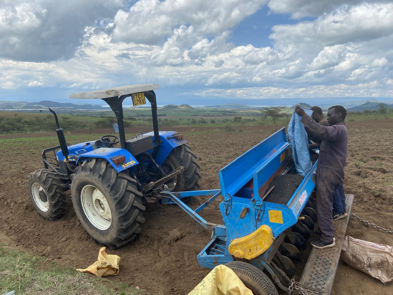 Workers loading a blue seed planter attached to a tractor on a field.
